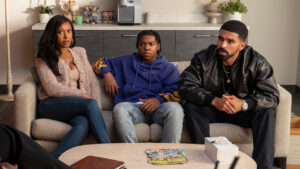 "Three people sit on a couch in a cozy, modern office talking to a therapist. Books, plants, and artwork decorate the room, suggesting a professional therapy or counseling session with a relaxed atmosphere."